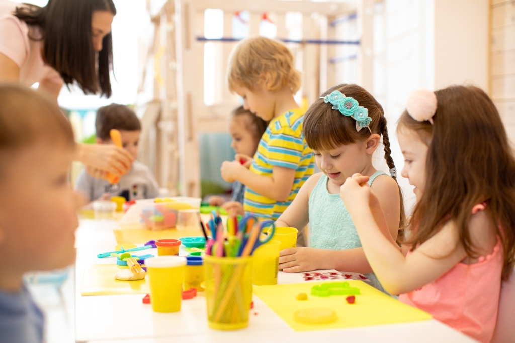 Group of kindergarten children playing with plasticine or dough. Little kids have a fun together with colorful modeling clay at daycare.